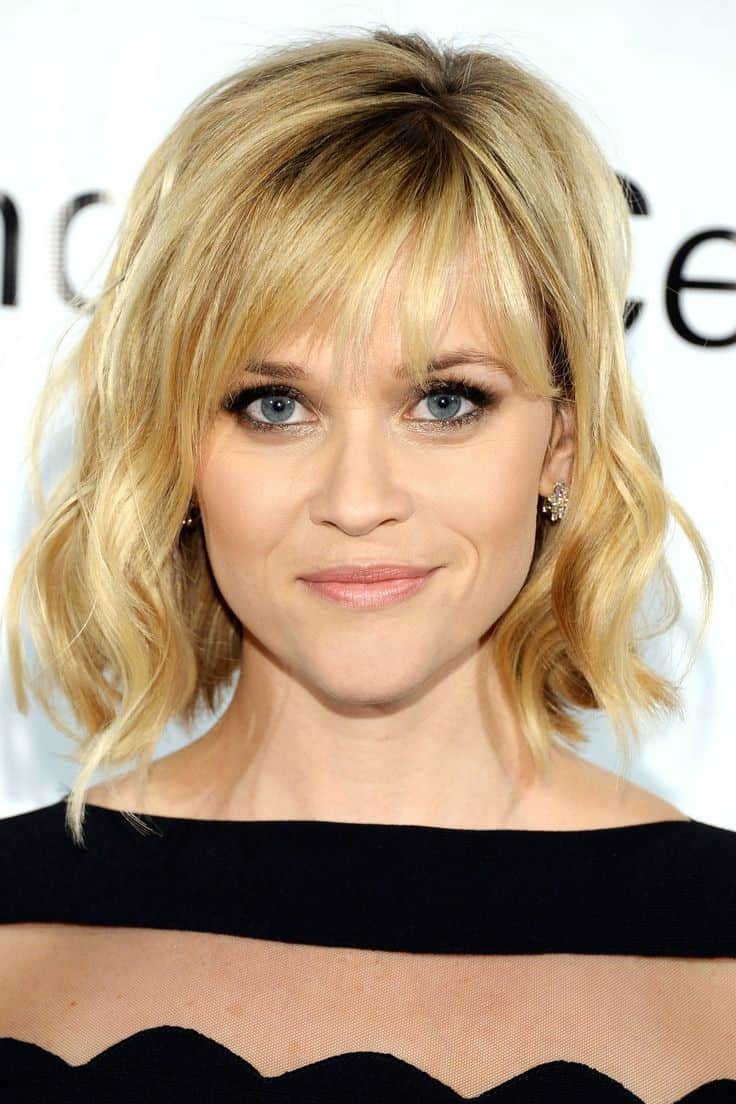 Wavy blonde bob with natural roots and brow-grazing bangs